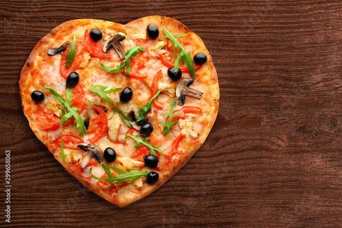 Tasty heart-shapped pizza on wooden background