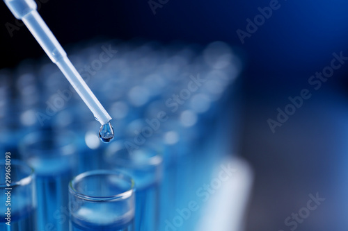 Dripping reagent into test tube with liquid sample on blurred background, closeup and space for text. Laboratory analysis photo
