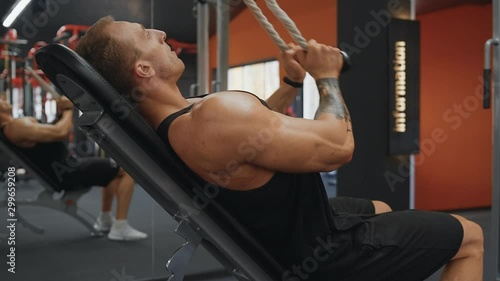 Bodybuilding concept. Muscular man doing cable rope triceps pull down exercise while working out in gym
