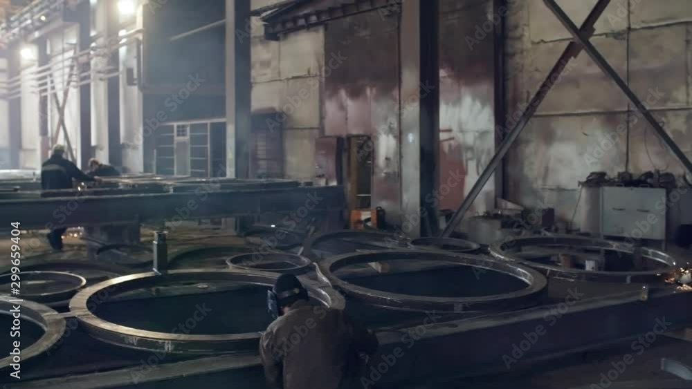 PAN shot of unrecognizable male workers welding and polishing round metal parts at fabrication facility PAN shot of unrecognizable male workers welding and polishing round metal parts at fabrication facility
