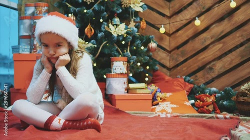 Disappointed little girl wearing Christmas costume sitting in lotos position over wooden christmas background, frowning her face.