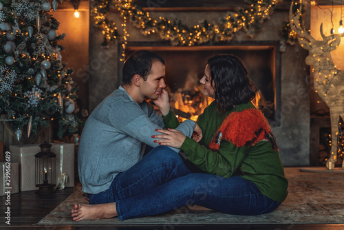 Loving couple sits by the fireplace with a Christmas tree in the New Year © Valeriia