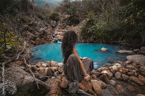 Beautiful young woman sitting at small mountain lake