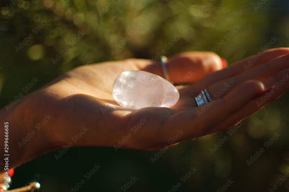 Female hand with transparent amethyst quartz yoni egg for vumfit, imbuilding or meditation. Shining crystal egg in hands on sky and sunrise background outdoors. Womens health concept.