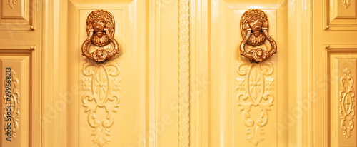 Two golden lion head door knockers on ornamental door, entry to a luxury villa home. photo