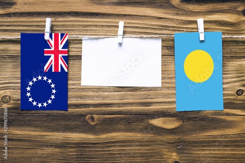 Hanging flags of Cook Islands and Palau attached to rope with clothes pins with copy space on white note paper on wooden background.Diplomatic relations between countries. photo