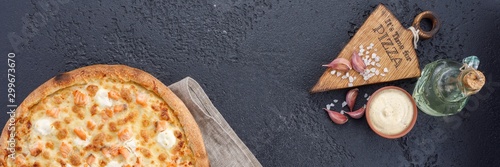 Pizza with salmon and cheese on a textural black background. Closeup. The concept of delicious food. View from above.