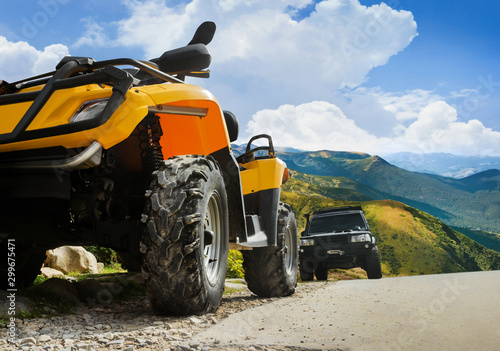 Atv and truck vehicles standing on a mountain landscape road.