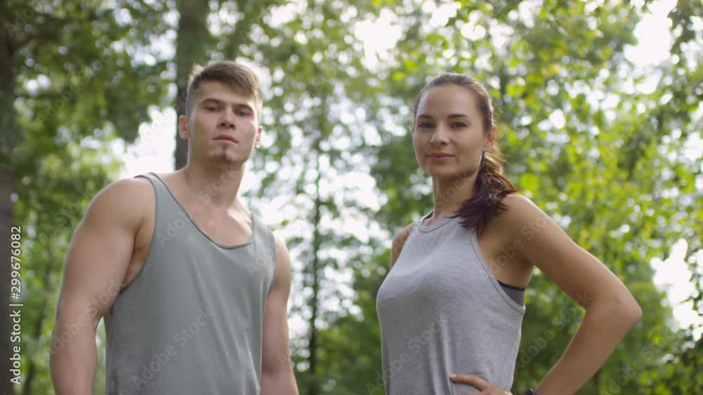 Waist up shot of confident male and female athletes in sportswear standing in park on summer day and looking at camera Waist up shot of confident male and female athletes in sportswear standing in park on summer day and looking at camera