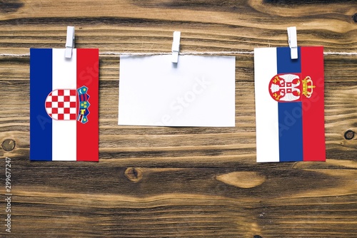 Hanging flags of Croatia and Serbia attached to rope with clothes pins with copy space on white note paper on wooden background.Diplomatic relations between countries. photo