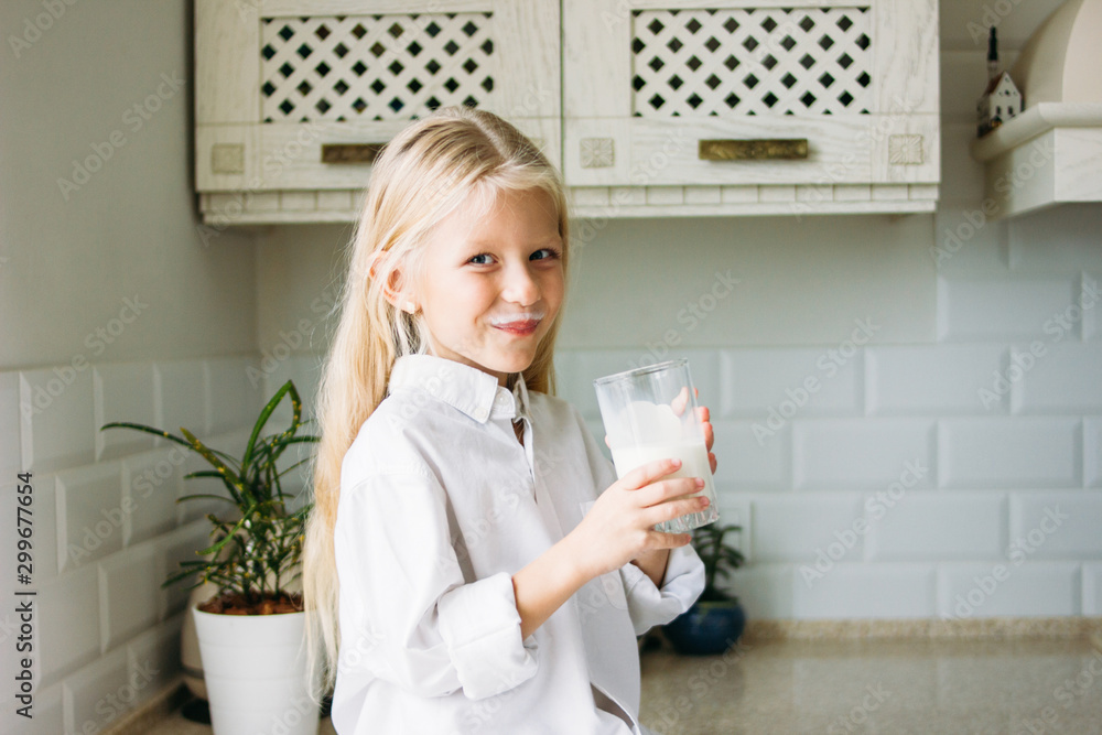 Happy blonde long hair little girl drinking milk in kitchen, healthy lifestyle