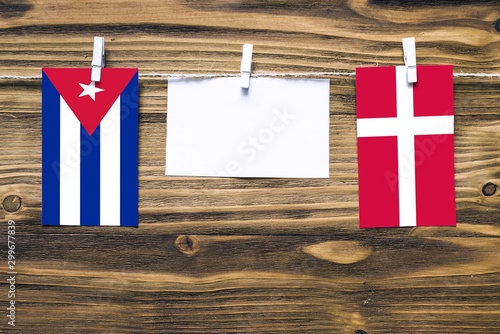 Photography Hanging flags of Cuba and Denmark attached to rope with clothes pins with copy space on white note paper on wooden background