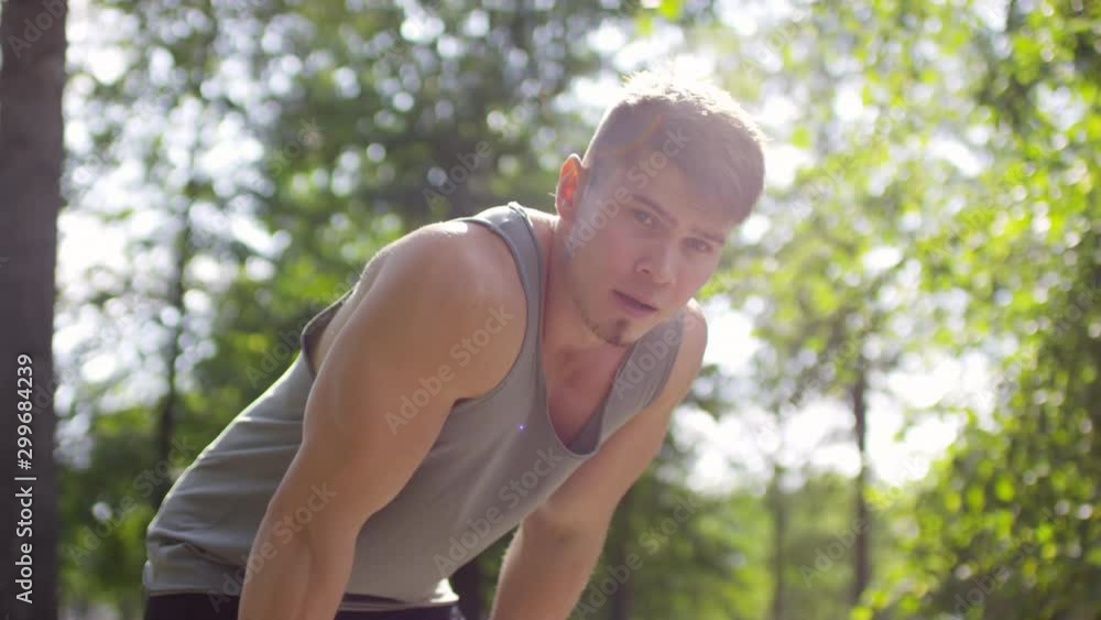 Young male athlete in sportswear running in park in the morning and then standing with hands on knees, heavily breathing and looking at camera while resting after exercising Young male athlete in sportswear running in park in the morning and then standing with hands on knees, heavily breathing and looking at camera while resting after exercising