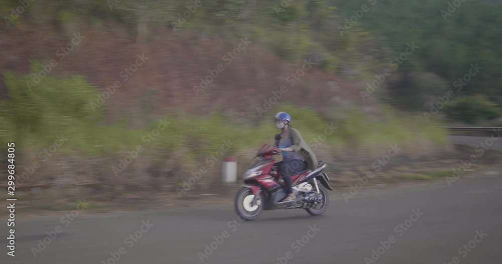 woman riding a moped on a rural road in Vietnam woman riding a moped on a rural road in Vietnam