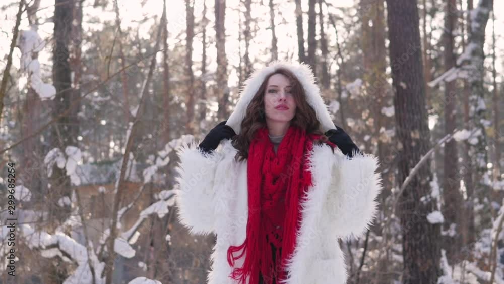 Attractive blonde in a white fur coat and red scarf posing on the background of a winter forest. Model in a white fur coat on a snowy background