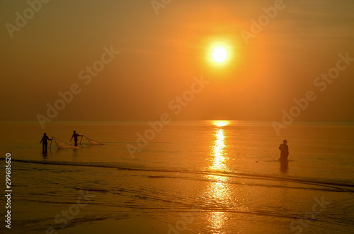 Tropical sunrise seascape with sun water reflection and fishermen silhouettes, Thailand.