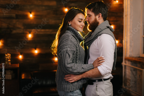Young married couple are hugging gently against the background of a wall with a festive garland.