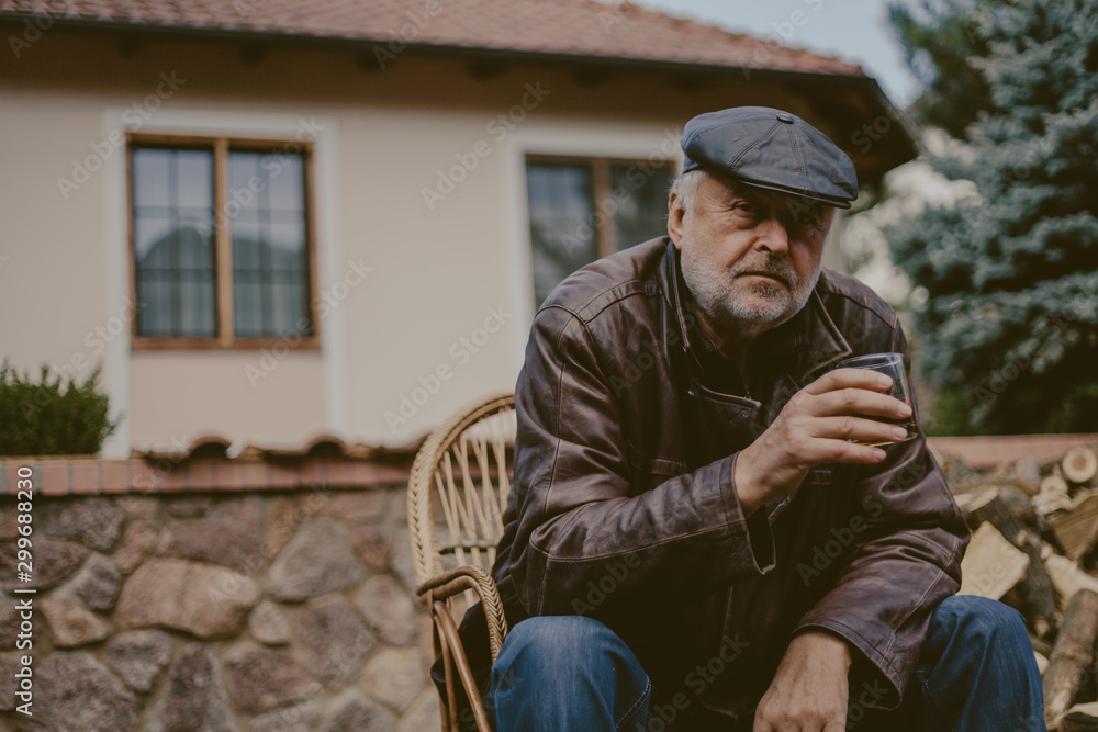 Elderly man with beard in leather jacket sits in yard