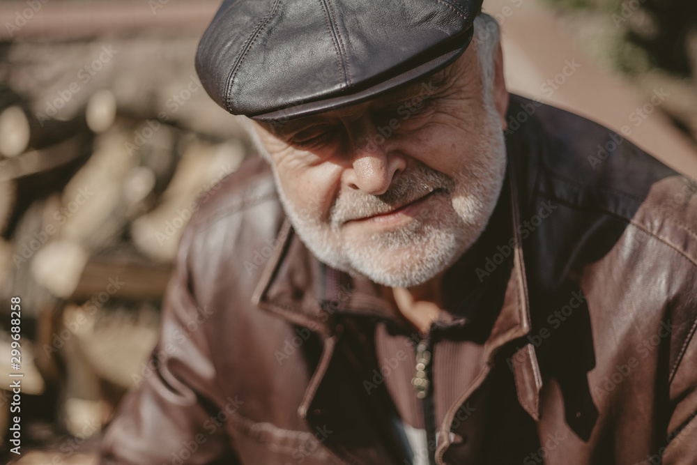 Handsome elderly man in leather cap sits in the yard