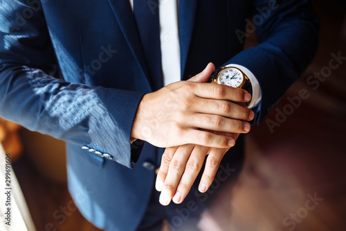 Men's wrist watch, the man is watching the time. Businessman clock, businessman checking time on his wristwatch. Groom's hands in a suit adjusting wristwatch, wedding preparations, groom accessories. © maxbelchenko