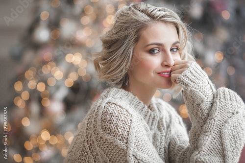 Beautiful blond woman on christmas background. Beauty near cristmas tree. Close up portrait of attractive female.