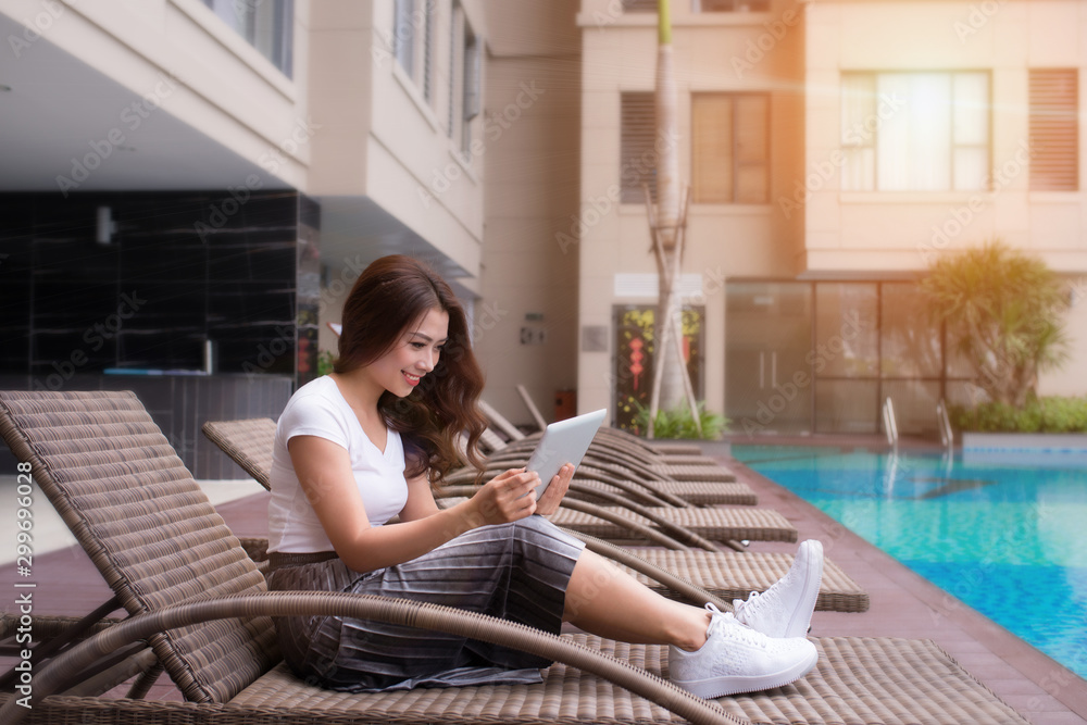 Young Asian Woman using her tablet by swimming pool Young Asian Woman using her tablet by swimming pool