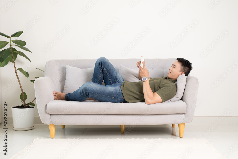 Relaxed man using a smart phone lying on an couch/sofa in the living room at home