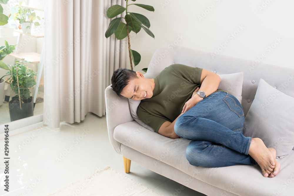 Man clutching his stomach from acute pain, lying on the couch