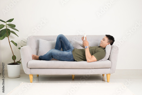 Relaxed man using a smart phone lying on an couch/sofa in the living room at home