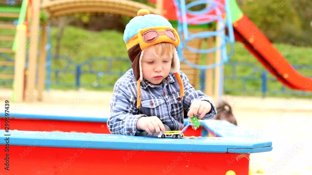 Stylish little boy playing in sandbox outside in fashionable kids clothes on playground. Happy family healthy children. Autumn style. Early child development. Kindergarten, urban city lifestyle Stylish little boy playing in sandbox outside in fashionable kids clothes on playground. Happy family healthy children. Autumn style. Early child development. Kindergarten, urban city lifestyle