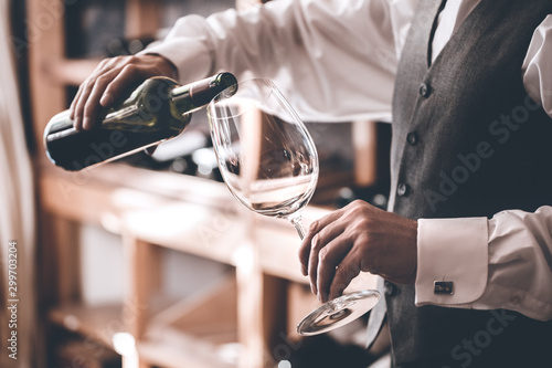 Sommelier Concept. Senior man standing pouring wine into glass close-up photo