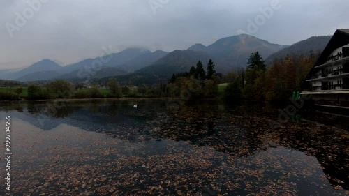 4K Left pan looking down calm lake covered with autumn leaves, reflection of Alps mountains in water photo