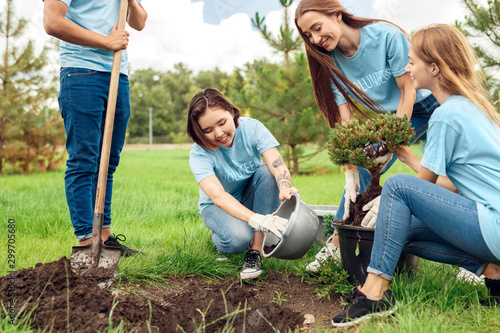 Volunteering. Young people volunteers outdoors planting trees putting fertilizer into hole smiling happy photo