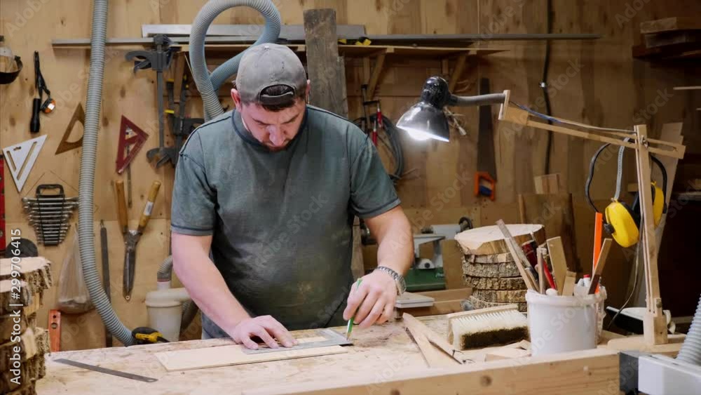 Adult male craftsman carpenter is measuring and marking a wooden detail at wood workshop. Camera moving on steadicam. Adult male craftsman carpenter is measuring and marking a wooden detail at wood workshop. Camera moving on steadicam.