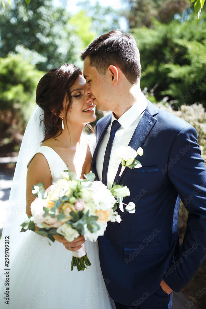 The bride and groom walk together in the park. Charming bride in a white dress, the groom is dressed in a dark elegant suit. Pretty bride and stylish groom. Wedding day. Marriage. The bride and groom walk together in the park. Charming bride in a white dress, the groom is dressed in a dark elegant suit. Pretty bride and stylish groom. Wedding day. Marriage.