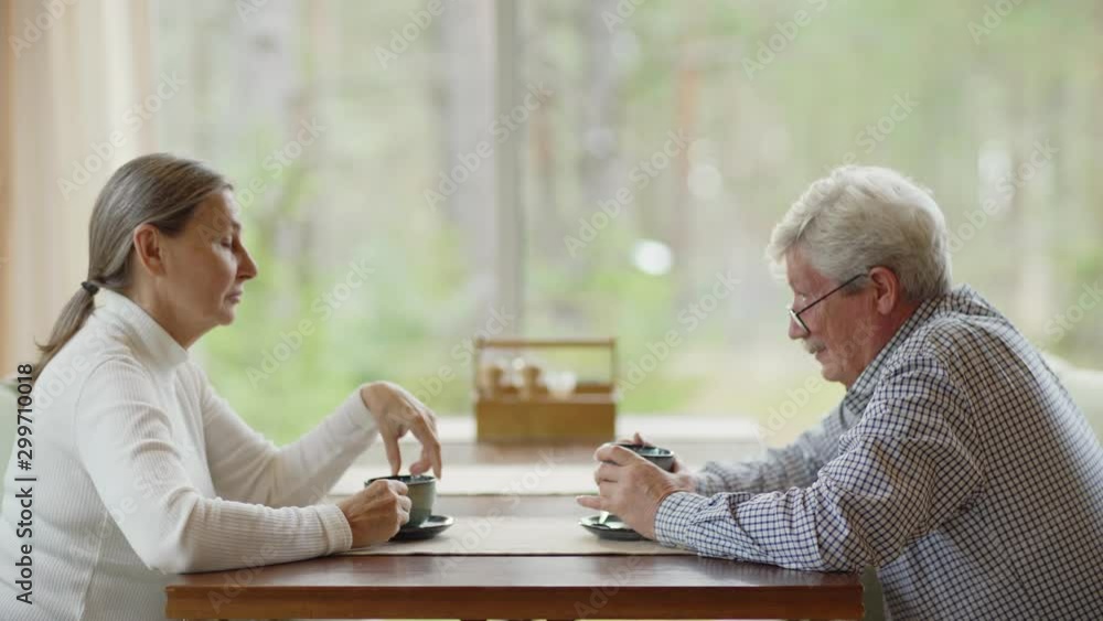Side view zoom in shot of senior man and woman sitting at table in cafe and talking over tea or coffee Side view zoom in shot of senior man and woman sitting at table in cafe and talking over tea or coffee