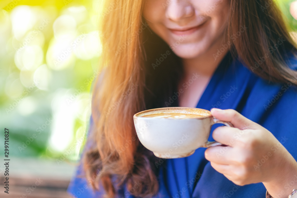 Closeup image of a beautiful asian woman holding and drinking hot coffee in the garden Closeup image of a beautiful asian woman holding and drinking hot coffee in the garden