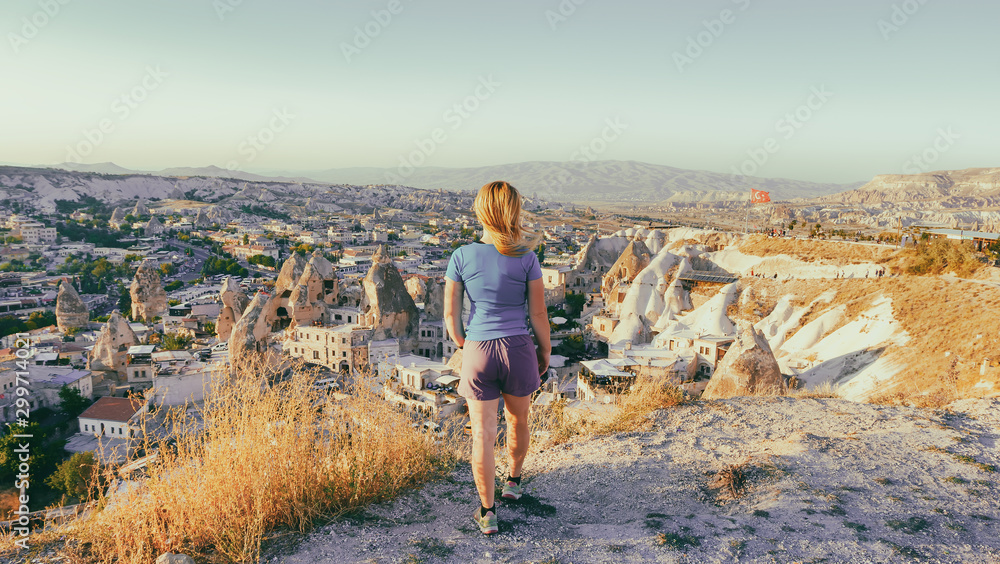View from the back of a girl stands on a hill and looks at synset in Cappadocia, Turkey.