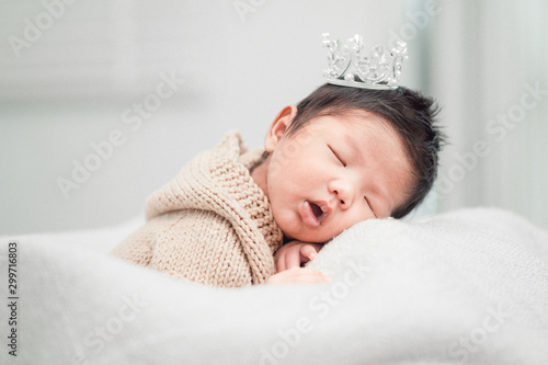 Newborn baby boy sleeping and wearing a silver crown.
