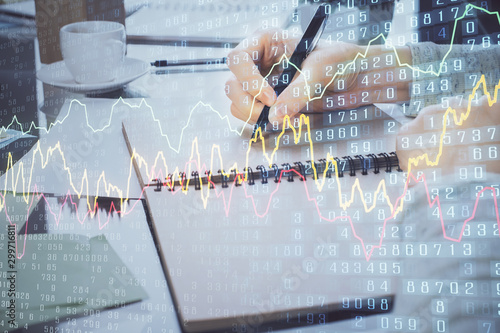 Hand taking notes in notepad. Forex chart holograms in front. Concept of research. Double exposure
