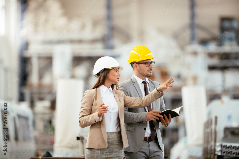 Businessman and businesswoman in factory. Man and woman in suits with helmets in factory discussing work. Businessman and businesswoman in factory. Man and woman in suits with helmets in factory discussing work.