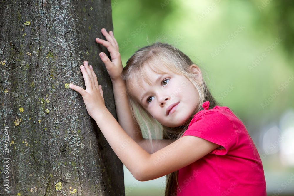 Portrait of a pretty little child girl standing near big tree trunk in summer park outdoors. Portrait of a pretty little child girl standing near big tree trunk in summer park outdoors.