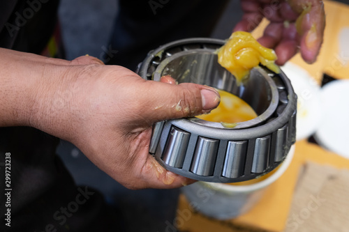 Senior worker putting lubricant lithium grease (NLGI 3) into wheel bearing for ten wheel truck car by hand at service station in Asia. Grease appearance is yellow. Maintenance and preventive concept.  photo