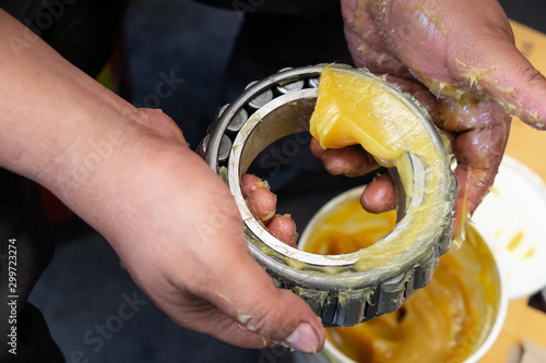 Senior worker putting lubricant lithium grease (NLGI 3) into wheel bearing for ten wheel truck car by hand at service station in Asia. Grease appearance is yellow. Maintenance and preventive concept.  photo
