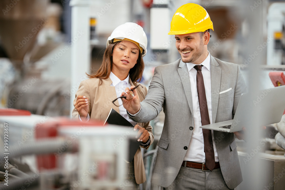 Businessman and businesswoman in factory. Man and woman in suits with helmets in factory discussing work. Businessman and businesswoman in factory. Man and woman in suits with helmets in factory discussing work.
