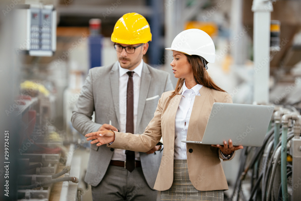 Businessman and businesswoman in factory. Man and woman in suits with helmets in factory discussing work. Businessman and businesswoman in factory. Man and woman in suits with helmets in factory discussing work.