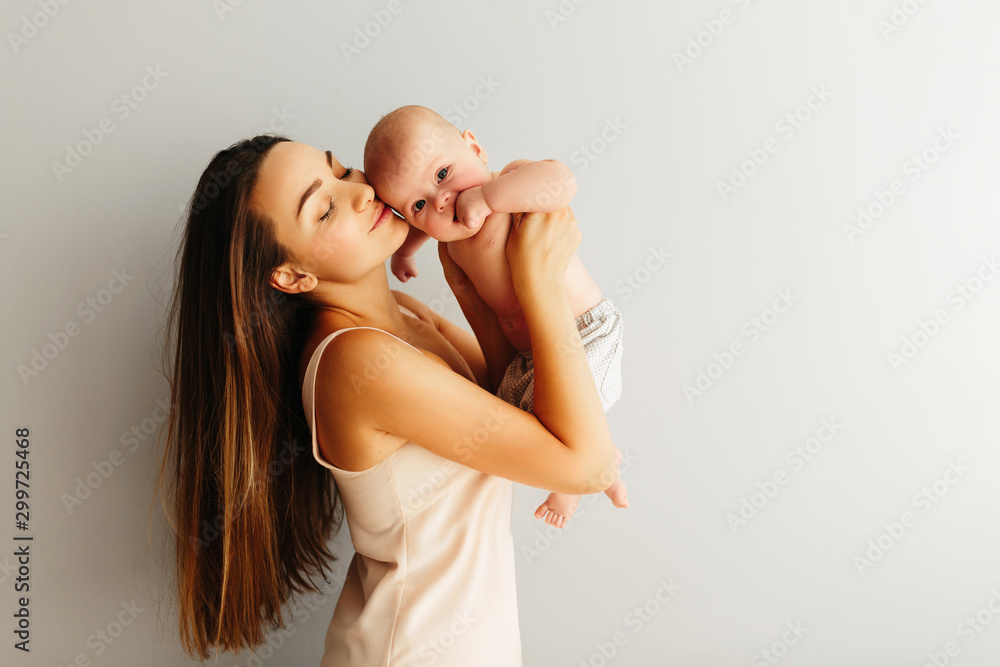 beautiful happy mother holds her baby on a plain light background. beautiful happy mother holds her baby on a plain light background.