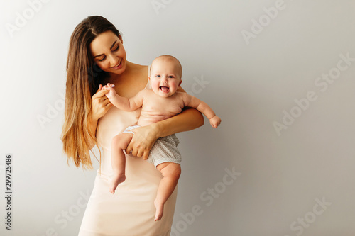 beautiful happy mother holds her baby on a plain light background. Child is smiling