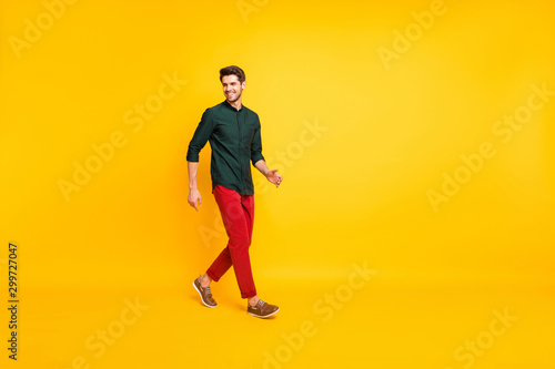 Turned full length body size photo of positive cheerful handsome guy walking towards empty space with cheerful smile isolated over vibrant color background
