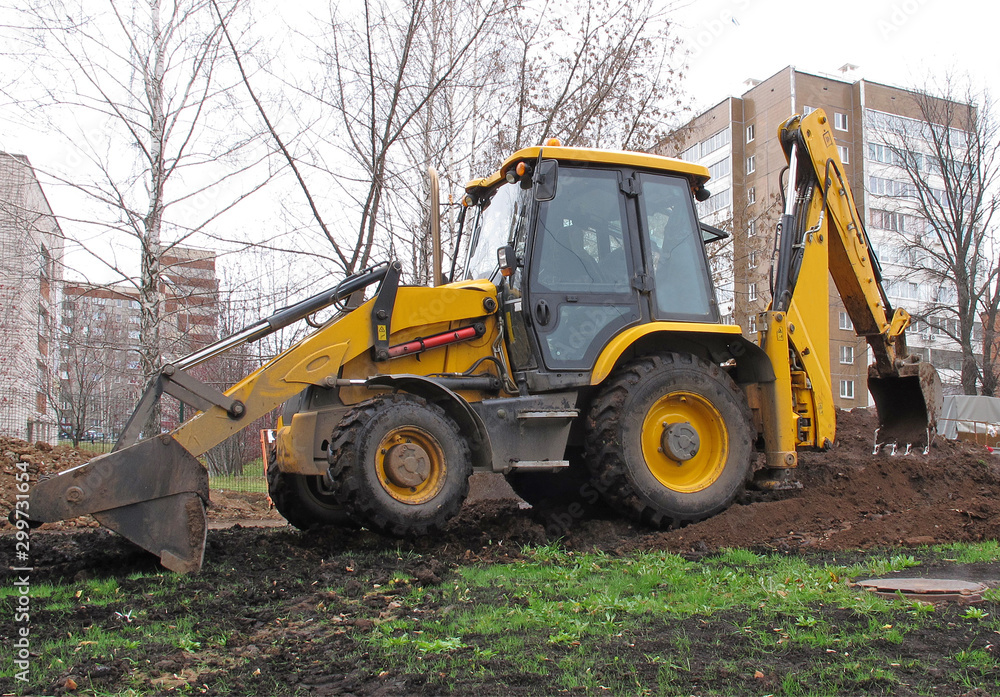 Yellow wheeled mini digger digs a trench in the city Yellow wheeled mini digger digs a trench in the city